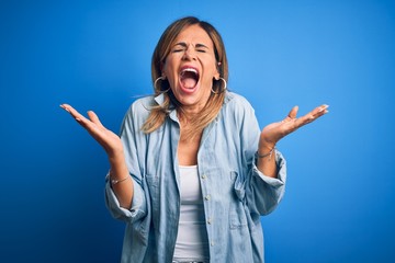 Middle age beautiful woman wearing casual shirt standing over isolated blue background celebrating...