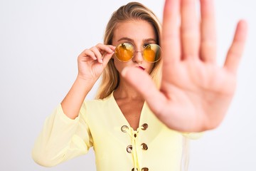 Young beautiful woman wearing yellow t-shirt and sunglasses over isolated white background with open hand doing stop sign with serious and confident expression, defense gesture