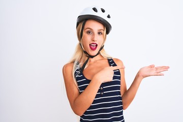 Young beautiful woman wearing bike helmet standing over isolated white background amazed and smiling to the camera while presenting with hand and pointing with finger.