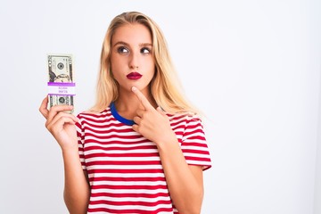 Beautiful woman wearing red striped t-shirt holding dollars over isolated white background serious face thinking about question, very confused idea