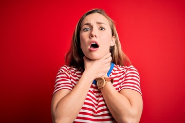 Young beautiful blonde woman wearing casual striped t-shirt over isolated red background shouting and suffocate because painful strangle. Health problem. Asphyxiate and suicide concept.