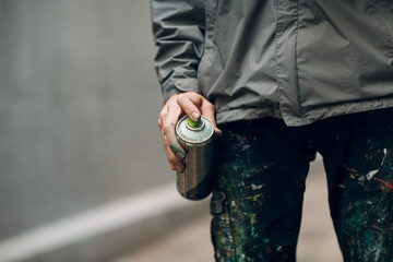 Graffiti artist in clothes stained with paint spray can in hand