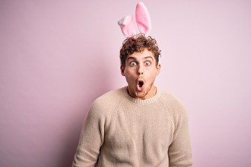 Young handsome blond man wearing easter rabbit ears over isolated pink background afraid and shocked with surprise expression, fear and excited face.