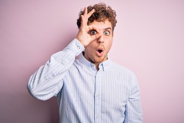 Obraz premium Young blond handsome man with curly hair wearing striped shirt over white background doing ok gesture shocked with surprised face, eye looking through fingers. Unbelieving expression.