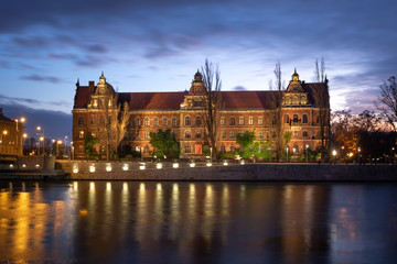 Fototapeta na wymiar Wroclaw, Poland. Illuminated historic building of National Museum reflecting in Oder river at dusk