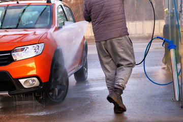 Man washes his orange car. Cleaning with a water jet at self-service car wash. Soapy water runs down. Сar wash in outdoors.