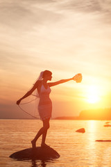 Bride on beach at sunset. Beautiful woman in white wedding dress with bouquet. Wedding by sea. A romantic trip to  tropical island in ocean. Happy girl