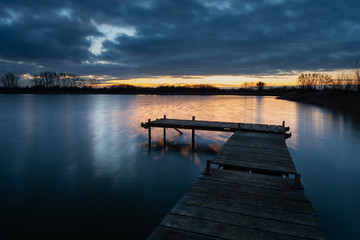 Fototapeta na wymiar Wooden deck bridge and evening clouds after sunset over the water, view in december day