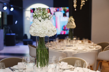 round served table with tablecloth with plates, glass, fork . festive table in restaurant decorated fresh flowers on birthday on wedding party. banquet table for guests in stylish cafe interior 