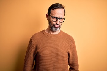 Fototapeta premium Middle age hoary man wearing brown sweater and glasses over isolated yellow background depressed and worry for distress, crying angry and afraid. Sad expression.