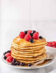 Sweet homemade pancakes with raspberries and blueberries on white plate.