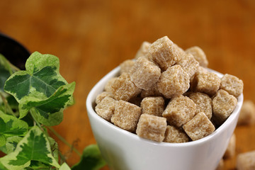 cup full of pieces of white and brown sugar on a wooden table with a blurred background