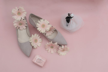 wedding concept. gerbera flowers, rings, beige shoes, newlywed figurine on a pink background.