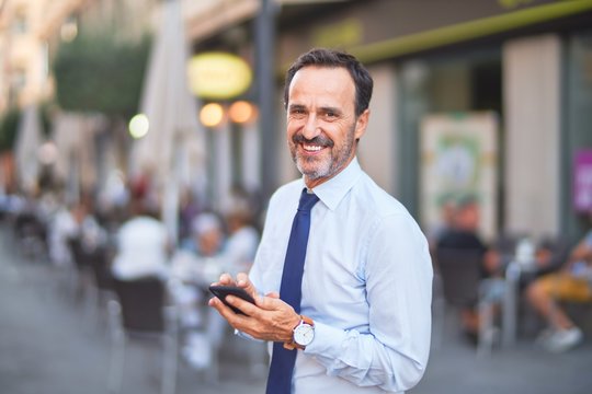 Middle age handsome businessman using smartphone on the street smiling