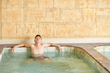 Asian Man relaxing with eyes closed enjoying hot tub alone in modern spa salon, horizontal shot