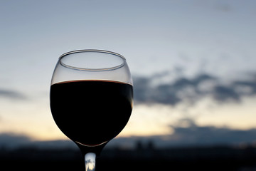 Silhouette of red wine glass on background of sunset sky with clouds. Concept of celebration, evening at resort, romantic dinner outdoors