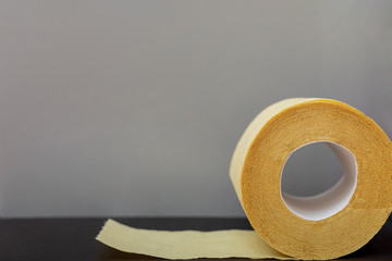 Roll of yellow toilet paper on a gray background. Copy space, flat lay.