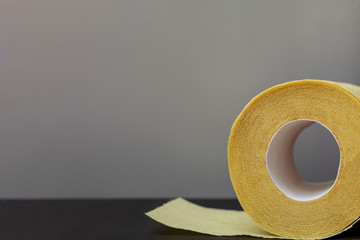 Roll of yellow toilet paper on a gray background. Copy space, flat lay.