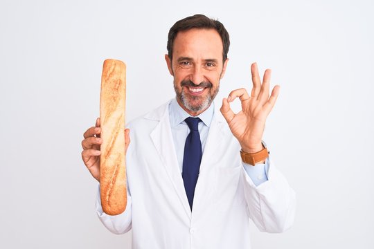 Middle age scientist man holding bread standing over isolated white background doing ok sign with fingers, excellent symbol