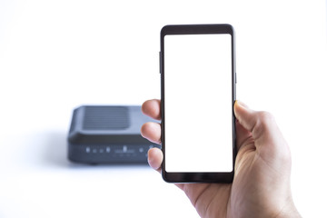 Hand holding white screen mobile phone and internet router in the background.