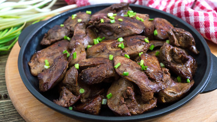 Fried chicken liver with young green onions in a cast-iron frying pan on a wooden background. Tasty healthy dish