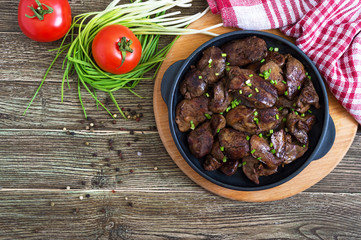 Fried chicken liver with young green onions in a cast-iron frying pan on a wooden background. Tasty healthy dish. Top view.
