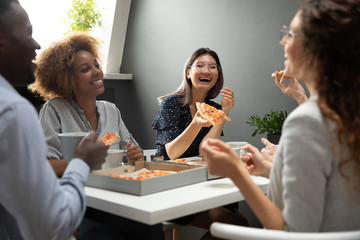 Smiling multiethnic colleagues have fun eating pizza in office