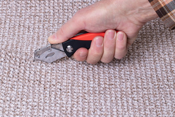People in handyman jobs. The hand of a craftsman cuts a carpet with a professional tool for laying...