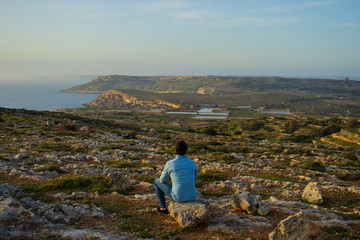 Fototapeta premium Man sitting and watching a beautiful scenery at Malta