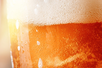 Close up gold background texture of yellow lager beer with froth and bubbles in glass, soft focus