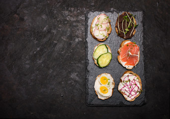 Cooking healthy vegetarian sandwiches. Assorted whole grain vegetable bruschettas with microgreen. Eating right concept, food background. Sandwiches with creamy cheese, cucumber, eggs, salmon, 