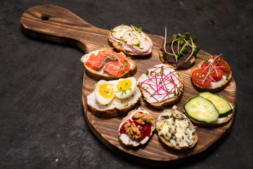 Cooking healthy vegetarian sandwiches. Assorted whole grain vegetable bruschettas with microgreen. Eating right concept, food background. Sandwiches on wooden cutting board.