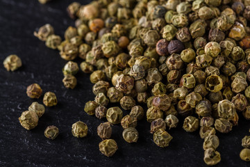 green peppercorns on dark slate stone background