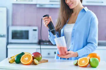 Woman uses hand blender to mixing fresh fruits for prepare diet smoothie in the kitchen at home