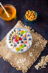 Oatmeal porridge with berries, fruits and honey on dark background. Oatmeal with raspberries, blueberries and almonds on burlap. Healthy breakfast