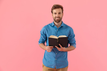 happy young guy in denim shirt smiling and holding book