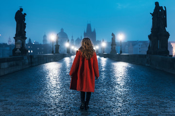 Female tourist walking alone on the Charles Bridge during the early morning in Prague, capital of Czech Republic