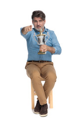 Positive casual man holding a trophy and pointing forward