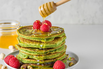 Matcha tea green pancakes. Pile of homemade pancakes with fresh raspberries, pistachios and flowing...