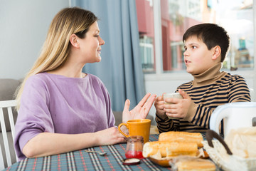 Young woman and son chatting at table with tea indoors