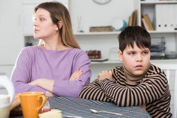 Upset mother and  unhappy son sitting after quarrel  indoors