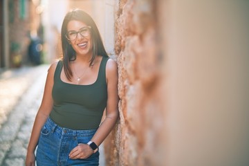 Young beautiful woman smiling happy and confident. Standing with smile on face leaning on the wall at the town stree