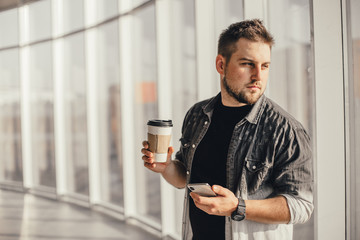 Young handsome man waitin for friend with cup of coffee and talking by phone