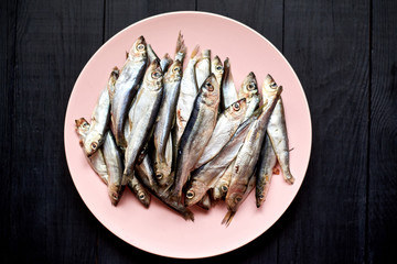 Raw fish sprats, herring on a plate on a dark wooden background.