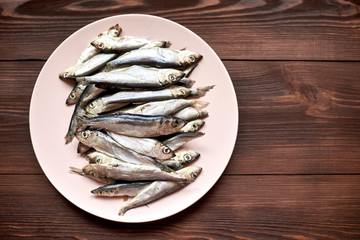 Raw fish sprats, herring on a plate on a wooden background.