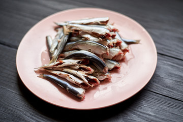 Raw gutted fish sprats, herring on a plate on a wooden background.
