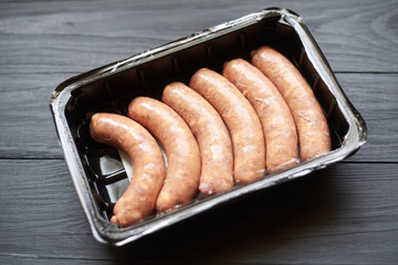 Raw grilled sausages in the package on a dark wooden background.