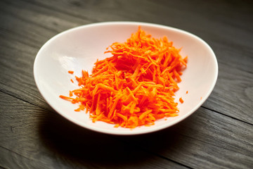 Grated carrots in a white plate on a dark wooden background.