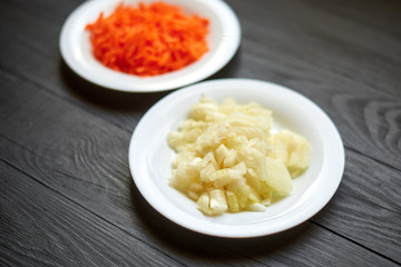 Grated carrots and chopped onions in a white plate on a dark wooden background.