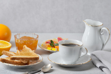 Coffee and toast with orange jam.  The concept of an elegant breakfast setting.  Oranges, cream, marmalade complete the composition.  Light background.  Close-up.